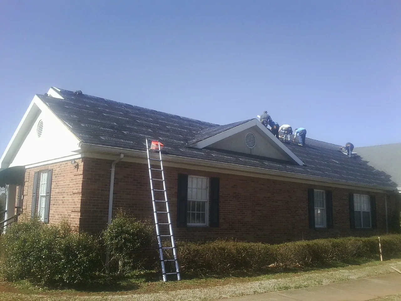 Crew tearing shingles off a brick ranch roof with a ladder set — Emergency Roof Repair work by our crew in Grayslake