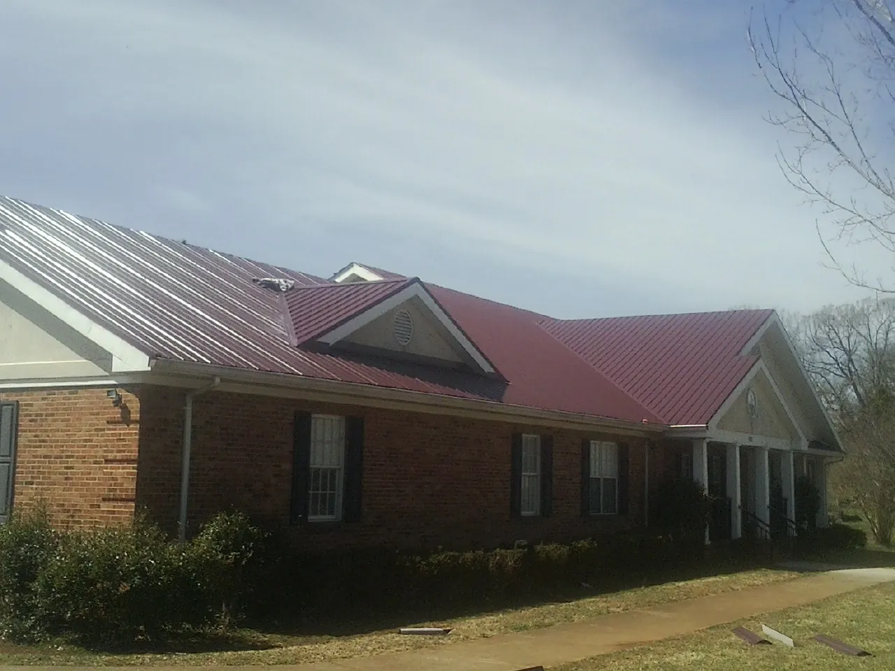 Red metal roof with gabled entries on a long brick building, from a Hail Damage Roof Repair job in Grayslake