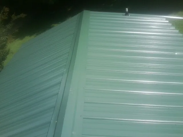New green metal panels meeting at the ridge of a roof — Flat Roof Repair work by our crew in Grayslake