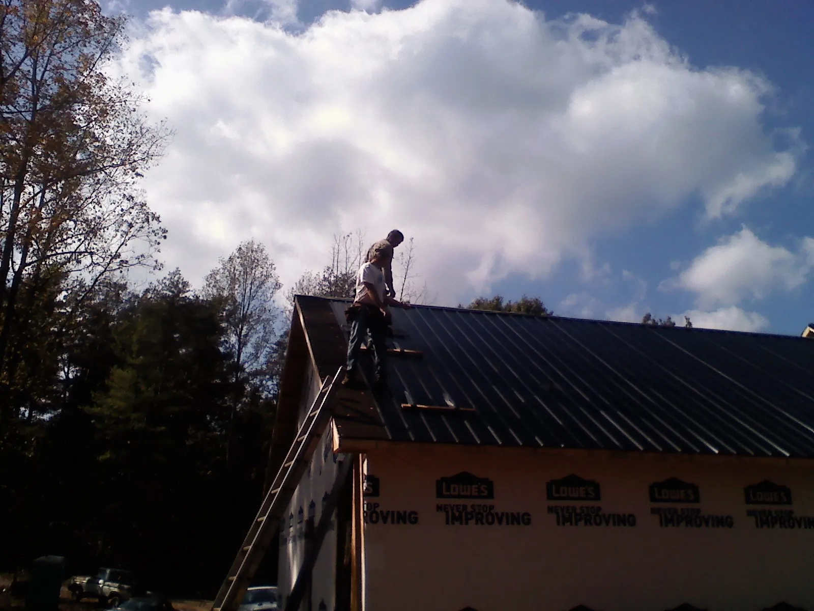 Roofer fastening dark metal panels high against a cloudy sky, from a Roof Inspection job in Grayslake