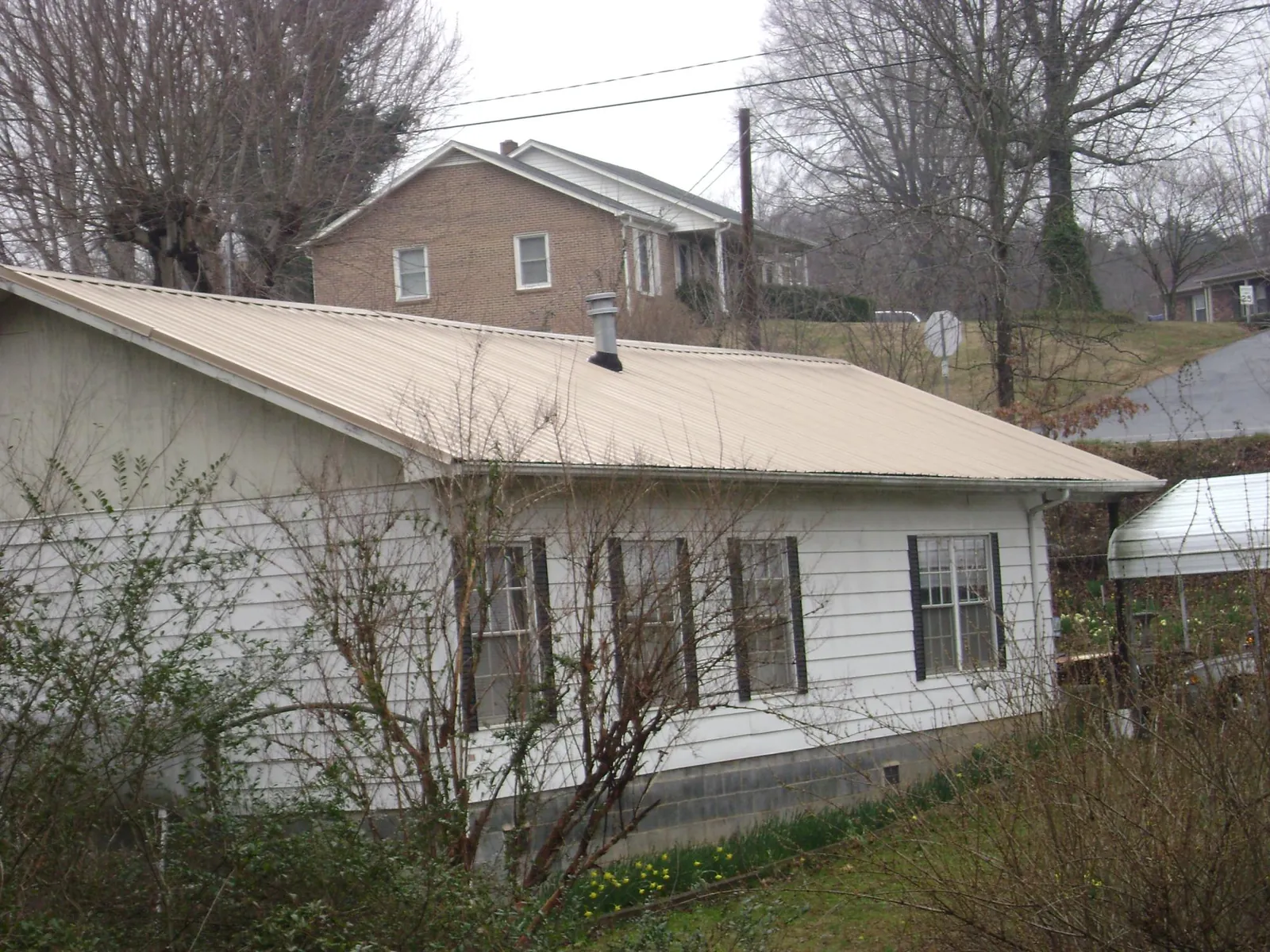 Tan metal roof on a white sided house set into a hillside — Commercial Roofing by Roofing Brothers in Grayslake